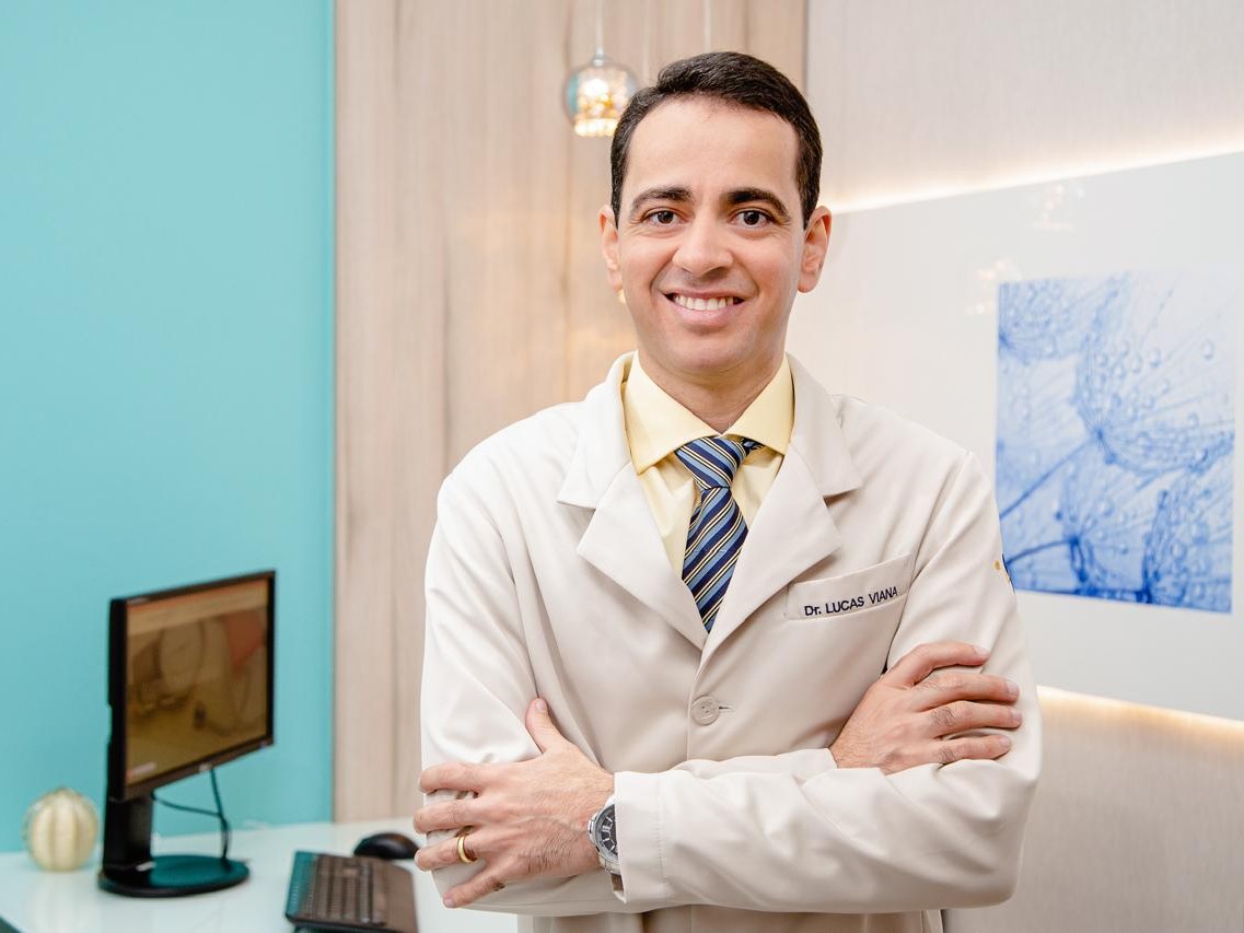 Dr. Lucas Viana de jaleco, de braços cruzados, no consultório da Gama Clínica