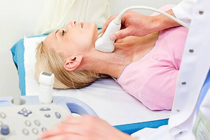 Transdutor de ultrassom deslizando sobre o pescoço de uma paciente durante um Doppler de carótidas