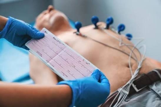 Paciente deitado com eletrodos no tórax durante um eletrocardiograma, com o traçado impresso em primeiro plano